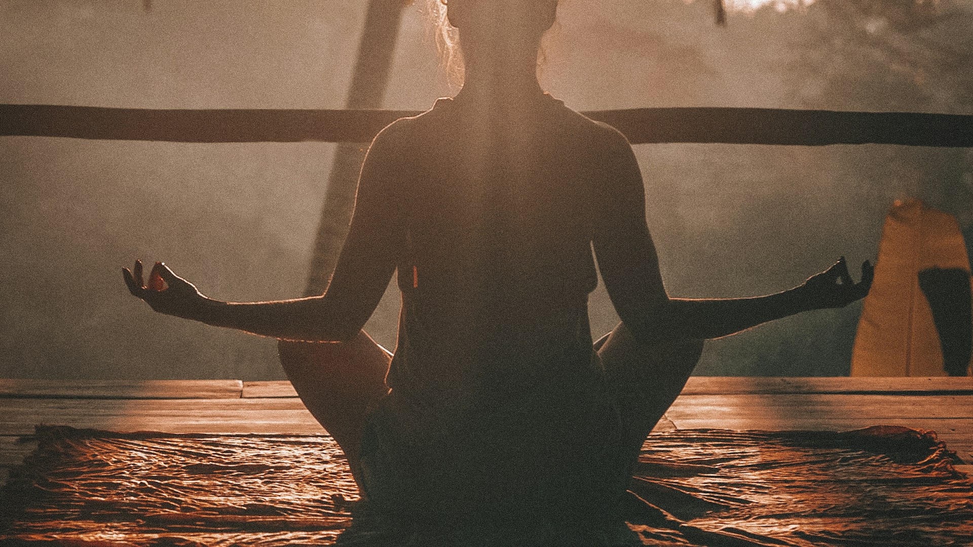 Woman meditating on cliff overlooking ocean at sunset